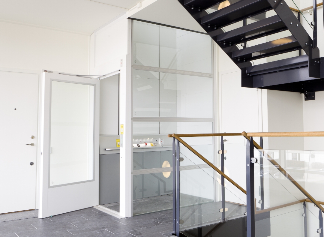 Teaserbild für "Öffentliche Lifte" Weiträumiger Flur in einem öffentlichen Gebäude mit moderner Treppe und weißem Fahrstuhl