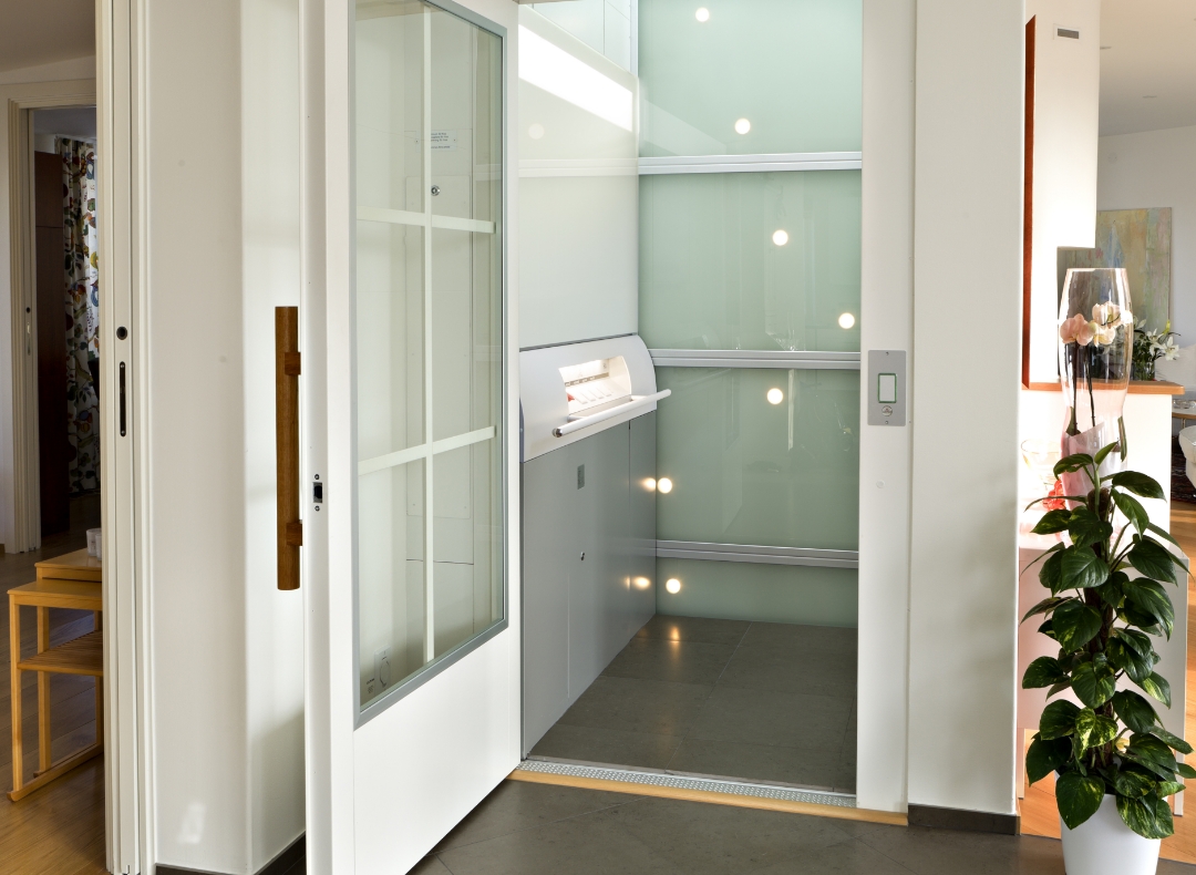 Teaserbild für "Lifte Privat" Blick in einen Lift mit offener Tür mitten in einem Wohnzimmer